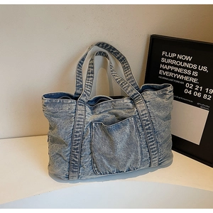 Macro shot of light blue washed denim tote bag with front pocket and frayed edge details