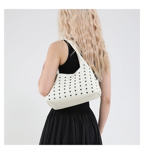 Detail view of the white rivet eyelet underarm bag styled by a model in a minimal setting