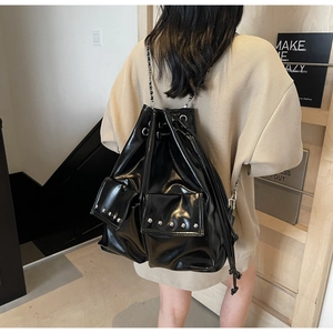 Black glossy drawstring backpack with silver rivet details worn by model in a cozy interior
