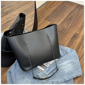 Large black tote bag with metal chain strap styled on denim jacket and a magazine