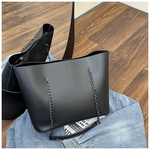 Detail of matte black tote bag featuring chain and leather strap on wooden floor