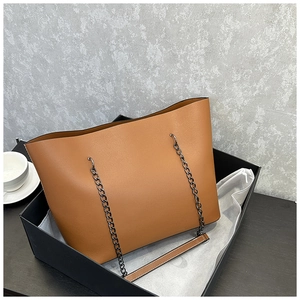 Close-up of caramel tote bag with chain strap in a black gift box with white dust bag