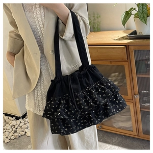 Detalle de volantes florales en bolso tote negro con cierre de cordón para un estilo casual