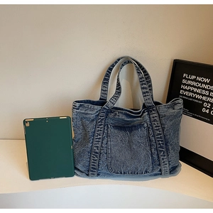 Detail of blue denim tote bag showing front pocket and washed fabric with tablet for scale