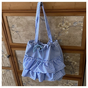 Detail of blue checkered tote bag featuring a tiered ruffle bottom and drawstring closure