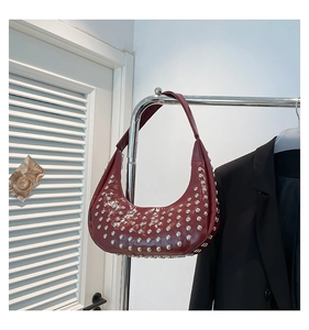 Detailansicht silberner Nietendetails auf dunkelroter Tasche aus glänzendem Leder