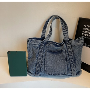 Detail of blue denim tote bag with front pocket showing large capacity next to a tablet