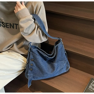 Close-up of deep blue denim tote bag featuring bronze metal studs and raw edge texture