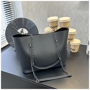 Macro shot of large black tote bag featuring matte leather texture and chain straps