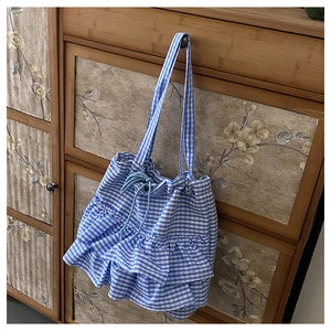 Detail of blue gingham tote bag with pleated ruffles and drawstring closure on cabinet