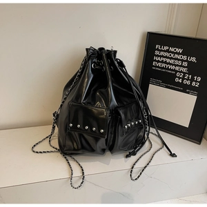 Detail of black glossy drawstring bucket bag with silver studs and chain strap