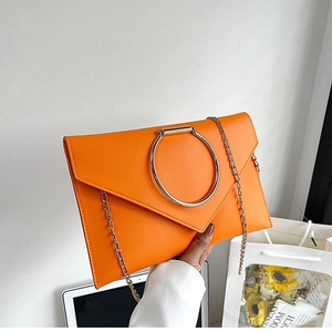 Détail d'une pochette enveloppe orange vif avec un grand anneau en métal argenté et chaîne