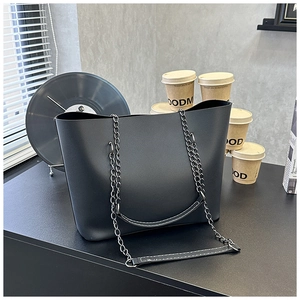 Detail of minimalist black tote bag with metal chain strap and matte leather texture