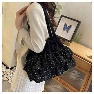 Detalle de bolso tote negro con estampado floral, capas de volantes y cierre de cordón