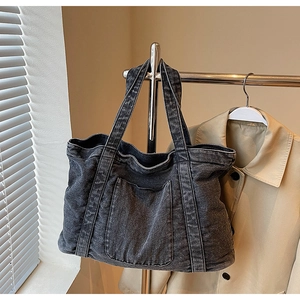 Detail of dark gray washed denim tote bag with visible stitching and front pocket