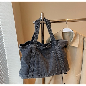 Detail of dark grey denim tote bag showing functional front pocket and double strap design