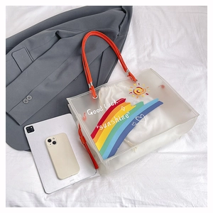 Detail of transparent PVC beach bag with rainbow print and orange handles for 2025