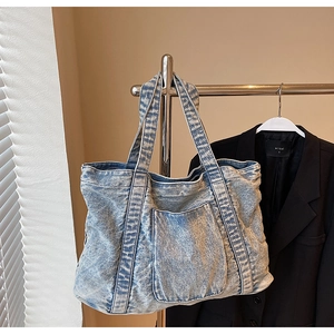 Detail of light blue acid wash denim tote bag with a large front patch pocket and handles