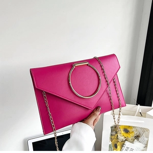 Gros plan d'une pochette fuchsia avec poignée anneau doré et bandoulière en chaîne