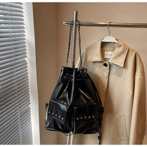 Close-up of black bucket bag with silver rivets and chain strap against a trench coat