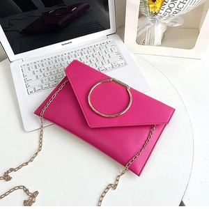 Détail de la pochette enveloppe fuchsia avec poignée en anneau doré et chaîne élégante
