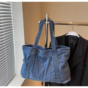Macro view of washed blue denim tote bag with front pocket hanging on a metal hanger