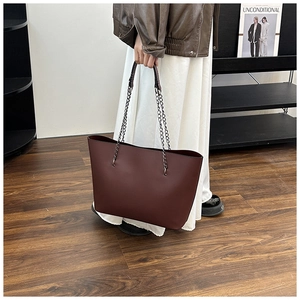 Detail of dark brown matte leather tote bag featuring chain straps on a model in-studio