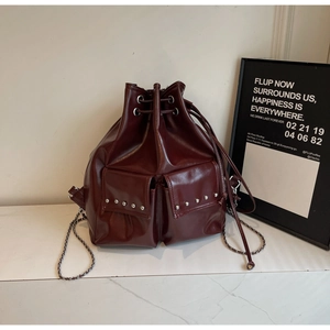 Detail of burgundy bucket bag featuring silver rivets and chain shoulder strap