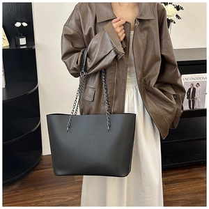Detail of a chic black tote bag with matte leather texture and metal chain strap