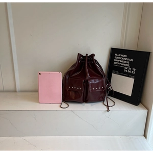 Detail of burgundy glossy bucket bag with silver studs and chain strap against white marble