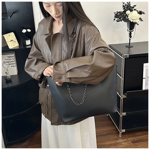 Close-up of black matte leather tote bag with metal chain on a female model