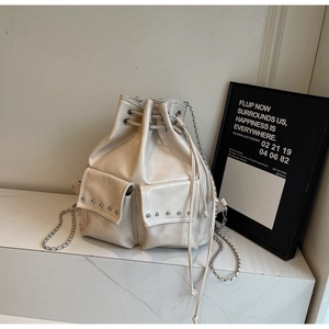 Detail of cream bucket backpack featuring silver rivets and drawstring closure with metal chain