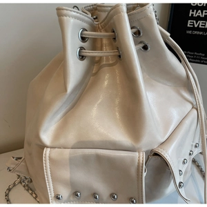 Close-up detail of cream bucket bag with silver rivets and drawstring closure