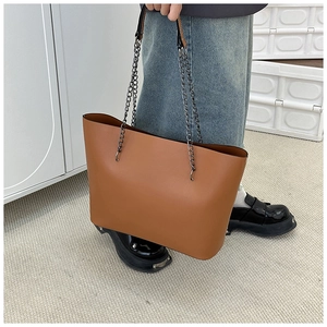 Detail of a brown large-capacity tote bag with metal chain strap and leather shoulder pad