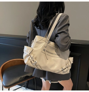 Macro detail of creamy white motorcycle tote bag with metallic buckles and zipper accents