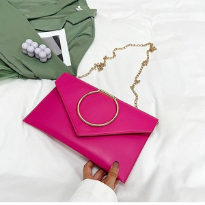 Détail de pochette enveloppe rose avec poignée anneau doré et bandoulière sur magazine