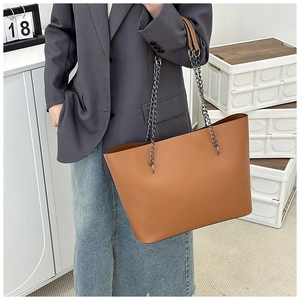 Close-up of a brown tote bag with silver chain straps worn by a model in a grey suit