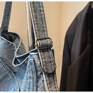 Detail of adjustable metal buckle and black D-ring on light blue denim tote bag
