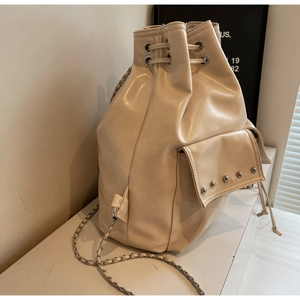 Detail view of beige bucket bag featuring silver rivets and chain woven shoulder strap
