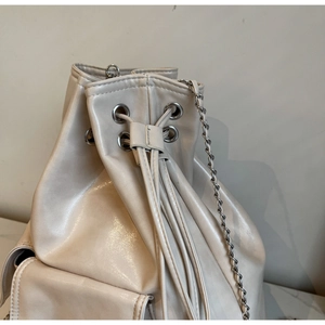 Close-up of beige drawstring bucket bag with silver metal eyelets and side chain strap