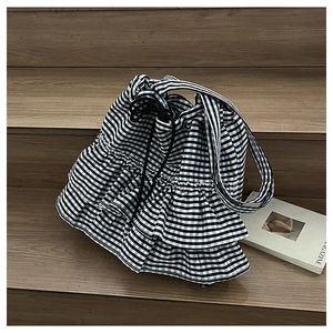 Detail of gingham drawstring bag featuring double-layered ruffle accents on wooden stairs