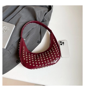 Detail der weinroten Halbmond-Tasche mit silbernen Nieten neben einem grauen Blazer