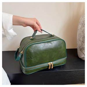 Close-up of vintage dark green leather makeup bag with dual gold zippers and smooth texture