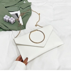 Détail de la pochette enveloppe blanche avec poignée anneau doré et chaîne sur tissu blanc