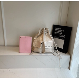 Detail of cream drawstring bucket backpack with stud accents and metal chain straps