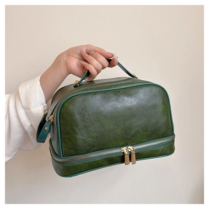 Detail view of dark green leather toiletry bag with double zippers and cracked texture