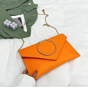 Détail d'une pochette orange vif avec une grande poignée en anneau doré et une chaîne