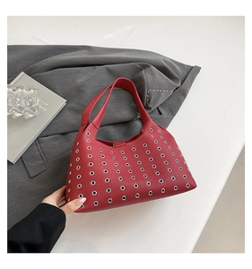 Close-up of red leather underarm bag featuring silver eyelet studs and grainy texture