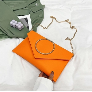 Détail d'une pochette enveloppe orange avec boucle dorée et fine bandoulière chaîne