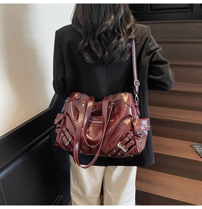 Detail of burgundy glossy leather tote bag with metal buckles on dark wooden stairs
